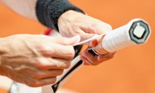 A player is fixing the grip on the handle of the racket
